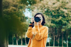 Teenage girl in orange sweater taking a picture with a camera