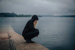 The image of a youth dressed in hoody sitting at the edge of a bay with head bowed looking into the water is to signify depression